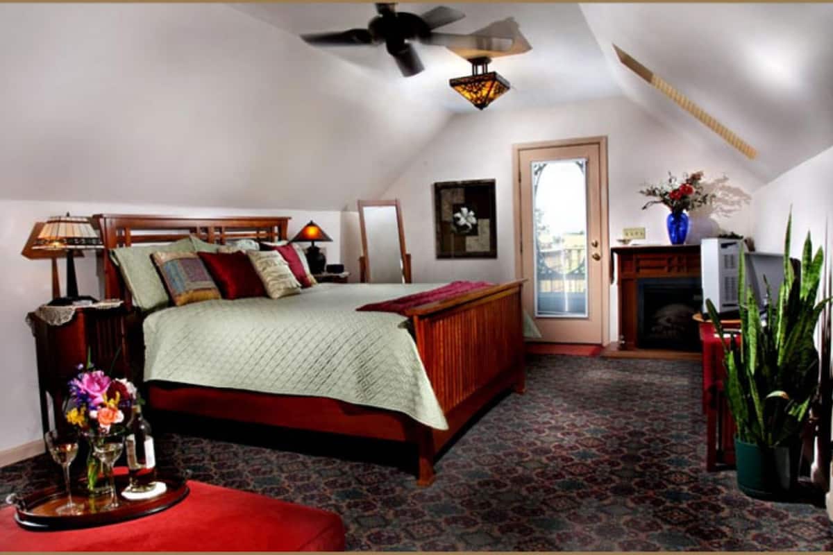 Une chambre à coucher comprenant un lit, un ventilateur de plafond, une cheminée et une porte donnant sur un balcon.