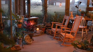 A cozy indoor seating area with a fireplace, wooden chairs, and various potted plants.