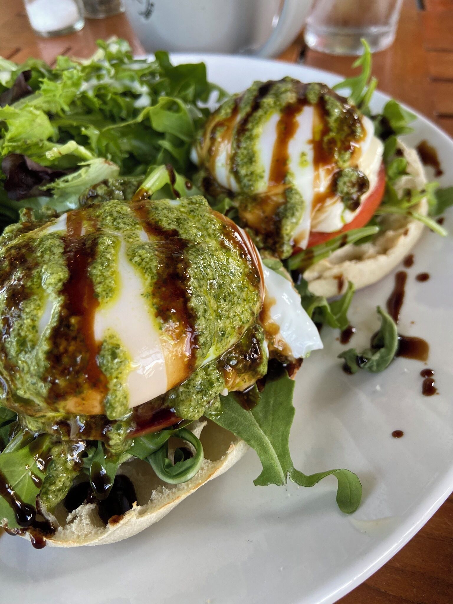 Un plato con un huevo pochado sobre una cama de vegetales verdes, cubierto con salsa verde y un chorrito de salsa.