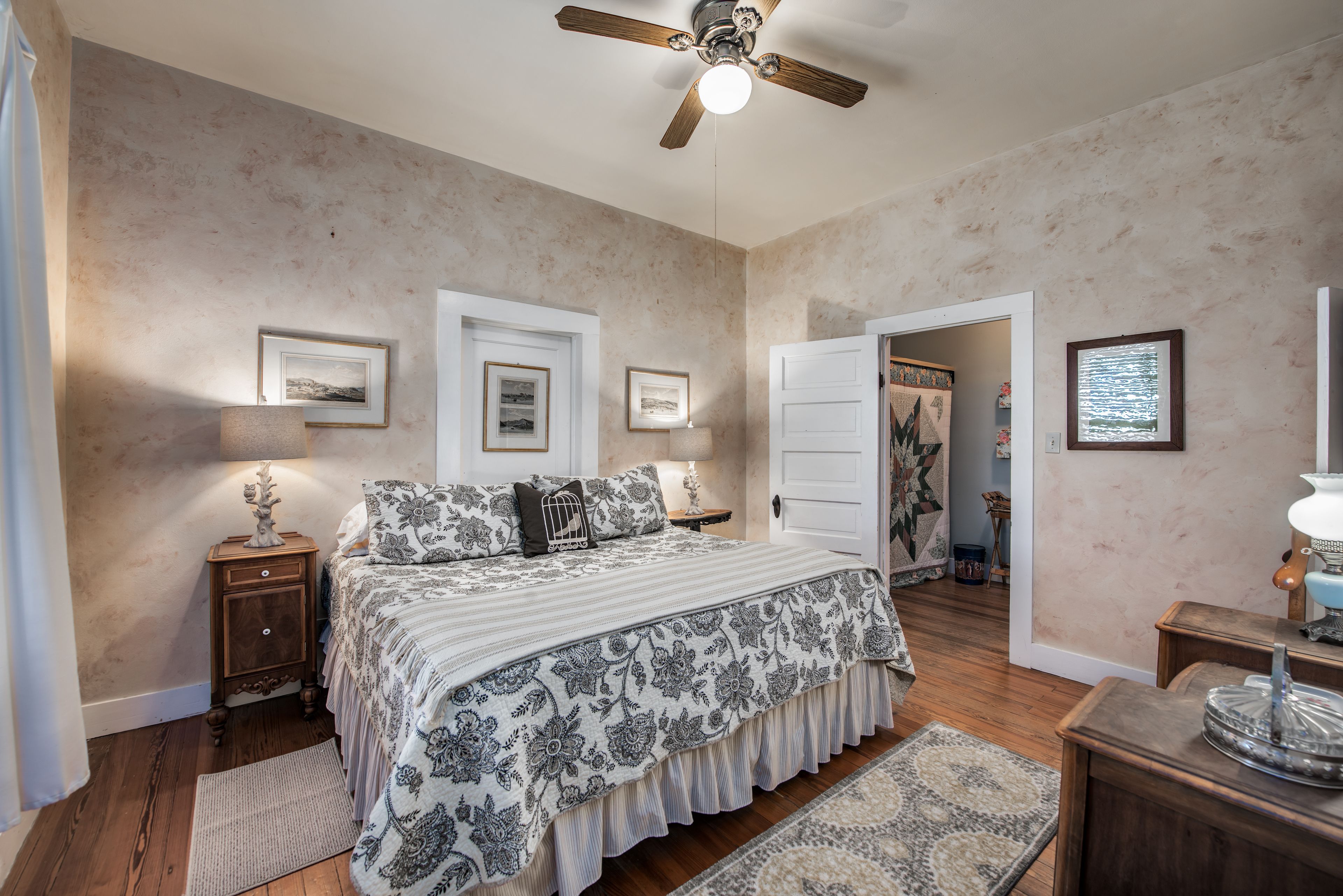 A bedroom with a bed, nightstands, a ceiling fan, and framed pictures on the walls.