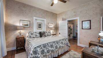 A bedroom with a bed, nightstands, a ceiling fan, and framed pictures on the walls.