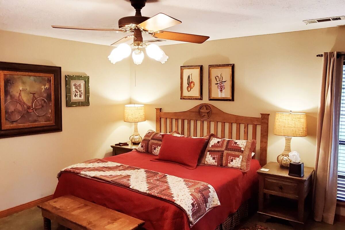 Un dormitorio con cama de madera, un banco, un ventilador de techo y dos lámparas fijadas a la pared.