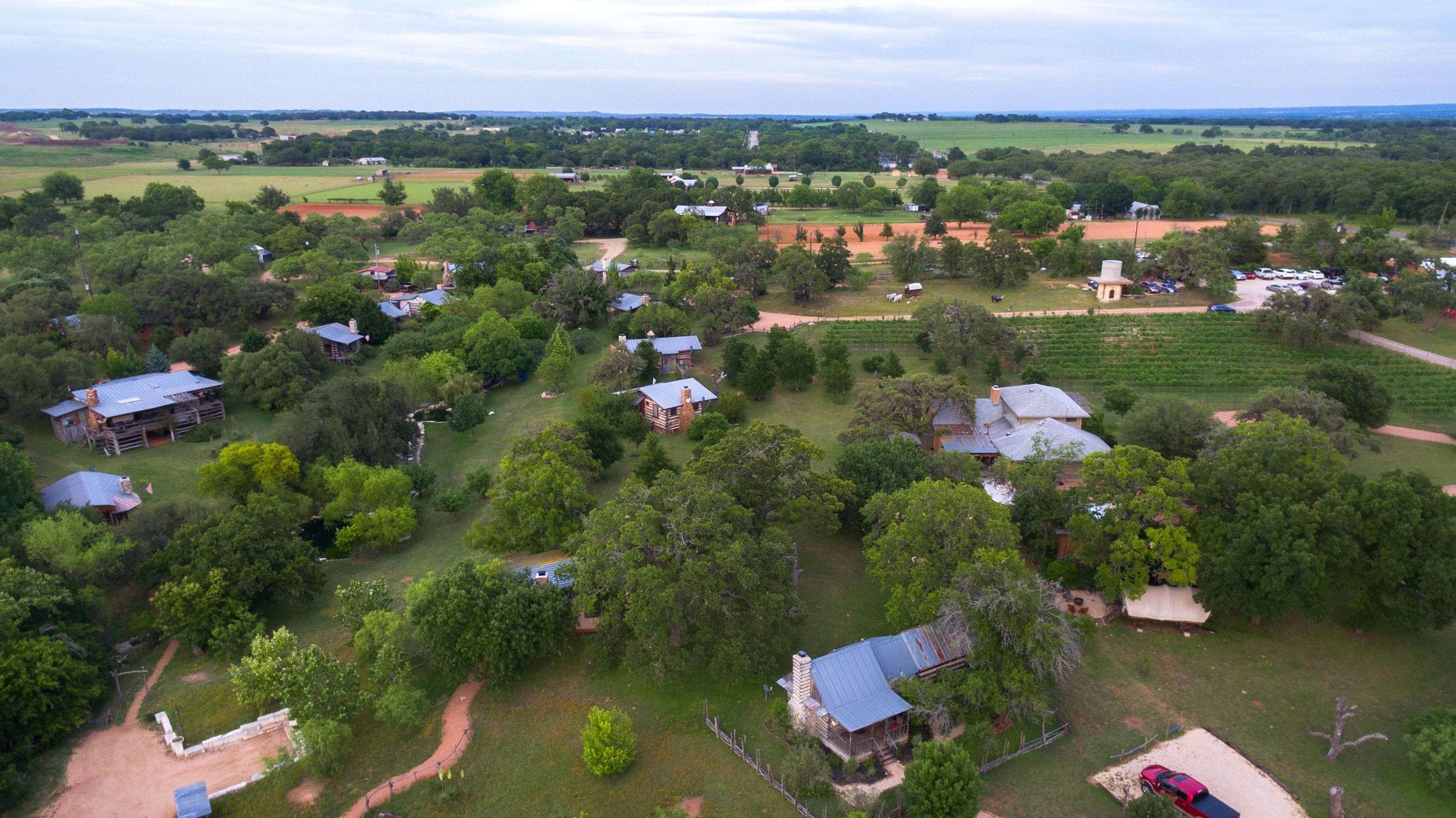 Vista aérea de uma área rural com várias casas cercadas por vegetação e campos.