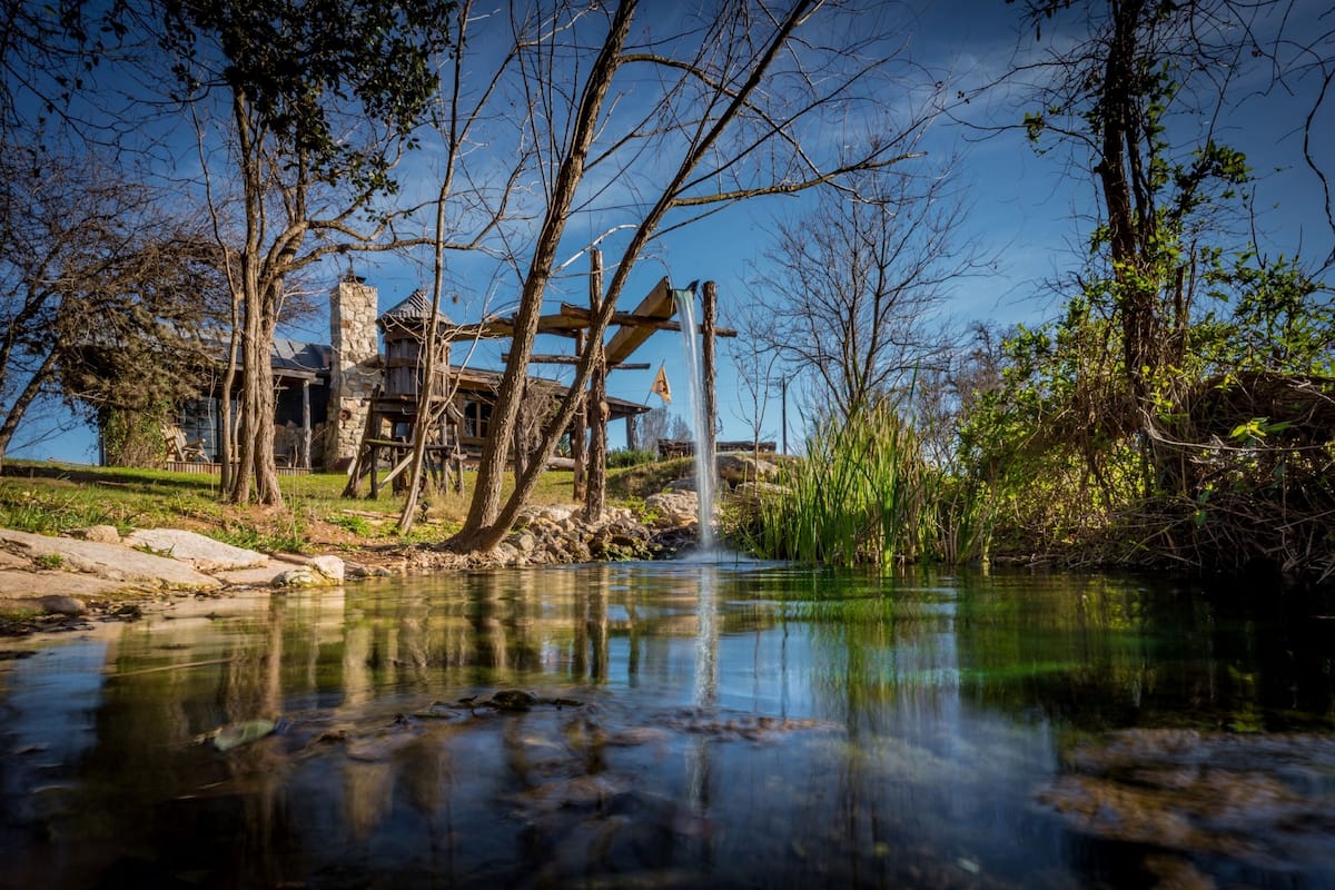 Un edificio rústico con una chimenea de piedra, vigas de madera y una cascada.