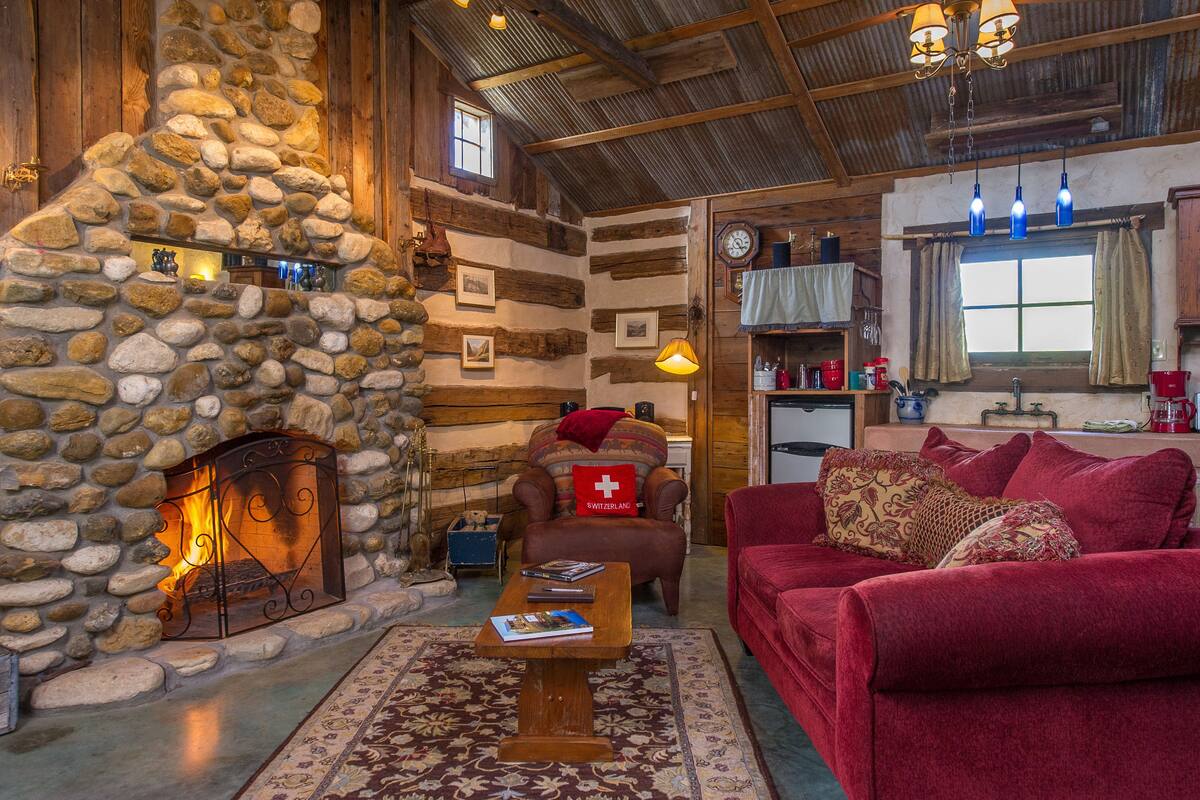 Una sala de estar acogedora con chimenea de piedra, un sofá rojo y una mesa de centro de madera.