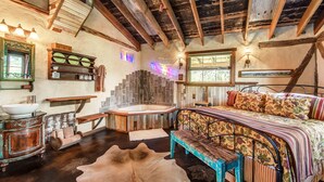 Un dormitorio rústico con una cama de madera, un ventanal amplio, una pared de piedra y techo de madera.