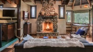 Una sala de estar acogedora con chimenea de piedra, vigas de madera, televisor y un espacio de descanso cómodo.