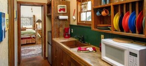 A narrow kitchen with wooden cabinets, a microwave, a sink, and a window with a view of the outside.