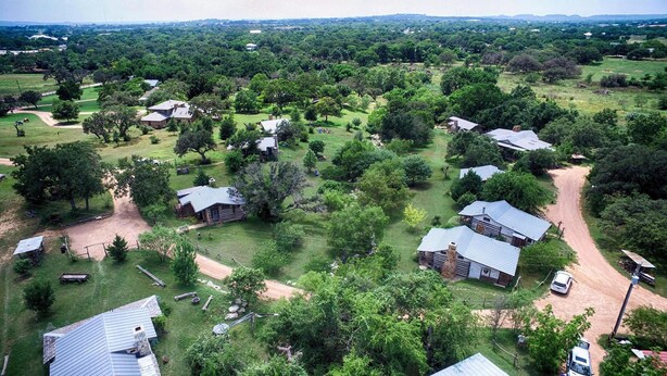 Una zona rural con varias cabañas y casas rodeadas de vegetación densa y campos abiertos.