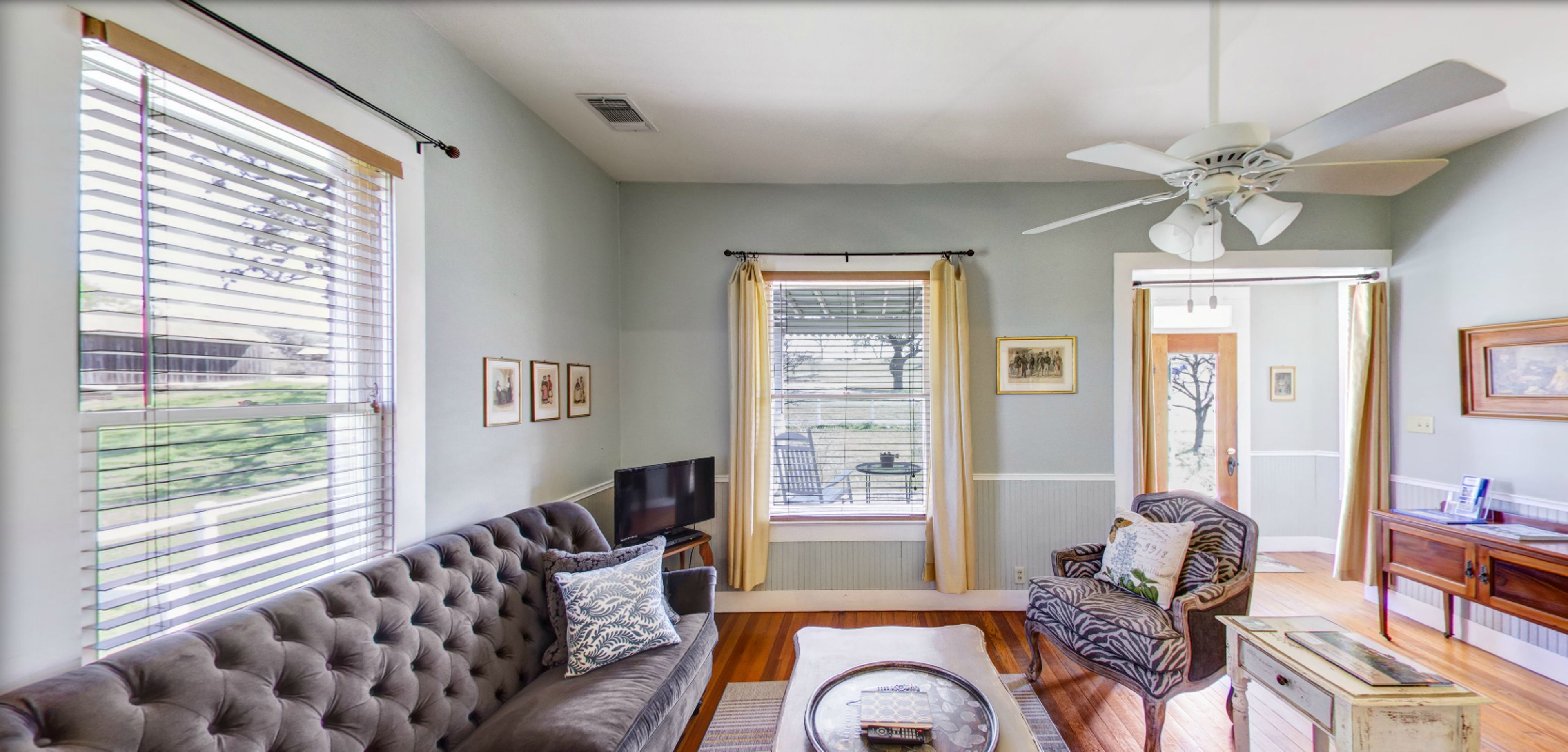 A living room with a tufted sofa, a zebra-patterned chair, a wooden coffee table, and a ceiling fan.