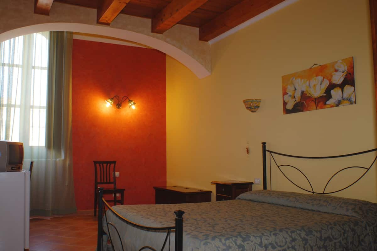 Un dormitorio con una cama, una silla, un escritorio, un televisor y un cuadro en la pared.