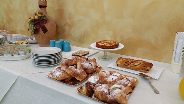 A buffet table with various pastries, including croissants and a cake, and a decorative vase with fruits and a ribbon. - B&B Triskeles (Syracuse)