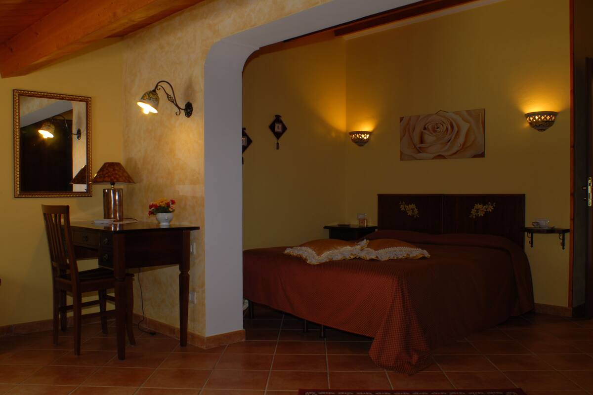 Un dormitorio con cama, escritorio, silla, espejo e iluminación en la pared.