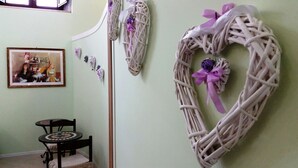 A room with a green wall, a framed painting, a wicker wreath with a purple bow, and a small round table with a chair. - B&B Triskeles (Syracuse)