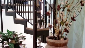 A staircase with a railing, a large vase with branches and flowers, and two potted plants on a patterned rug. - B&B Triskeles (Syracuse)