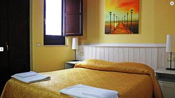 Una camera d'albergo con un letto, una finestra, un quadro e un comodino.