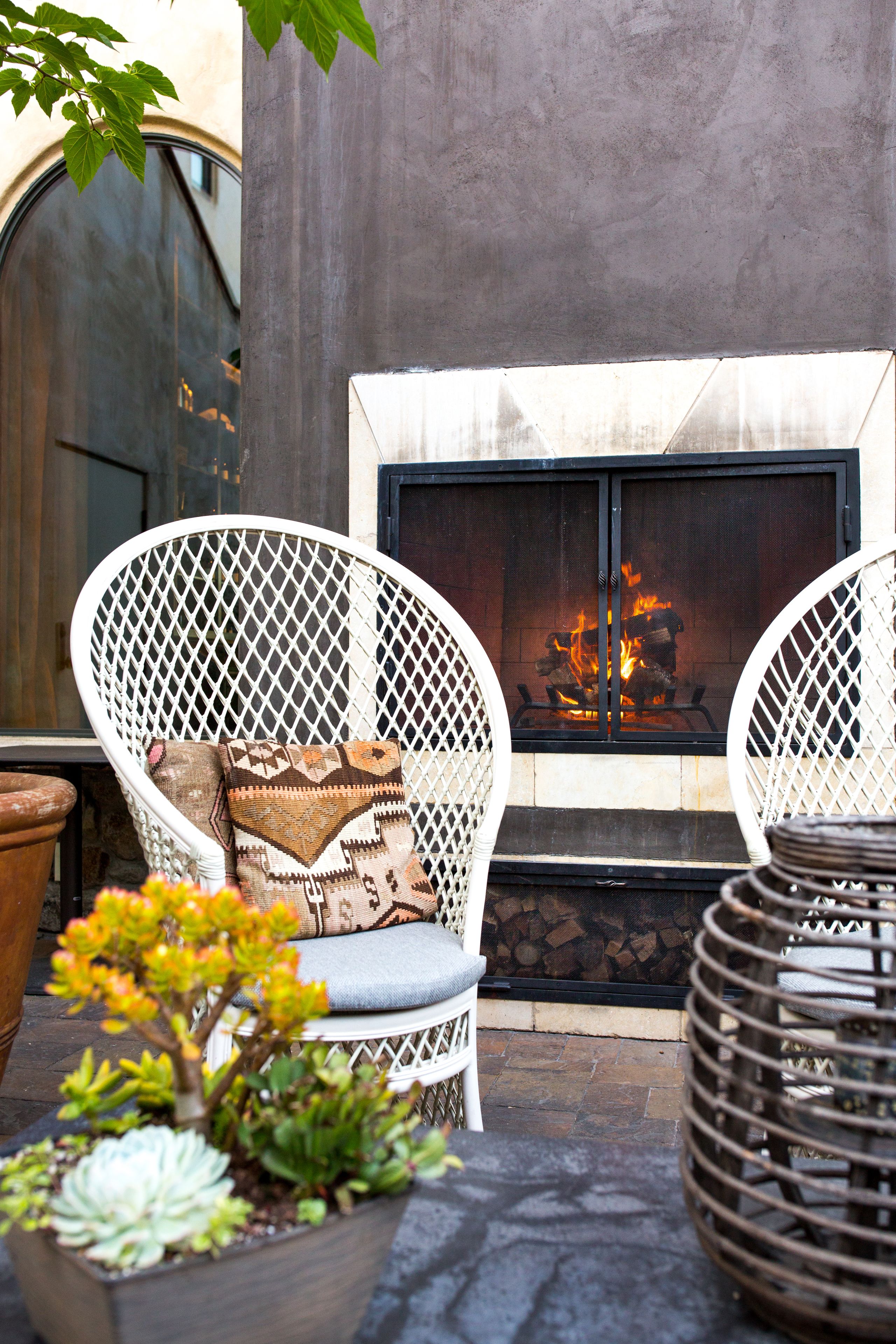 A cozy outdoor seating area with wicker chairs, a fire pit, and potted plants.