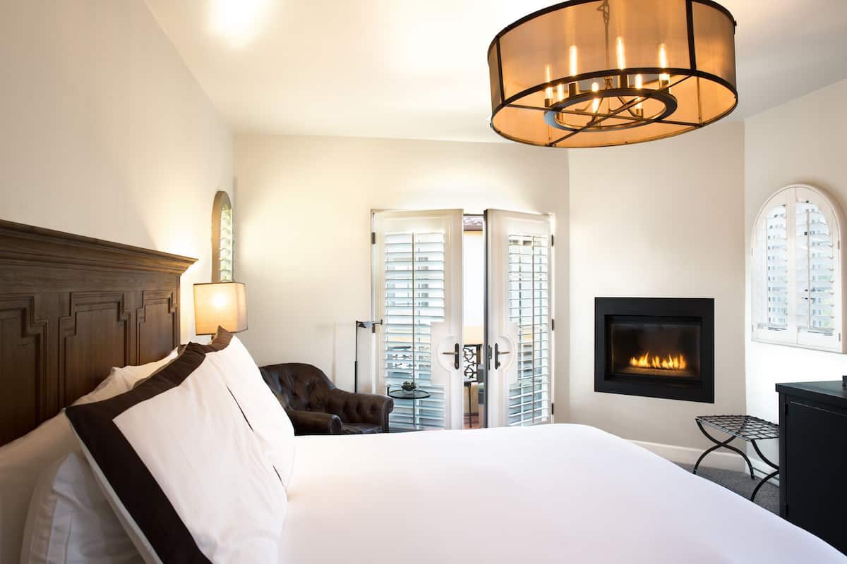 A hotel room with a large bed, a fireplace, a chandelier, and a view through a window.