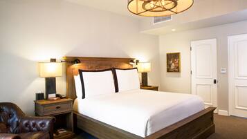 A hotel room with a large bed, two bedside tables with lamps, a leather armchair, and a wooden headboard.