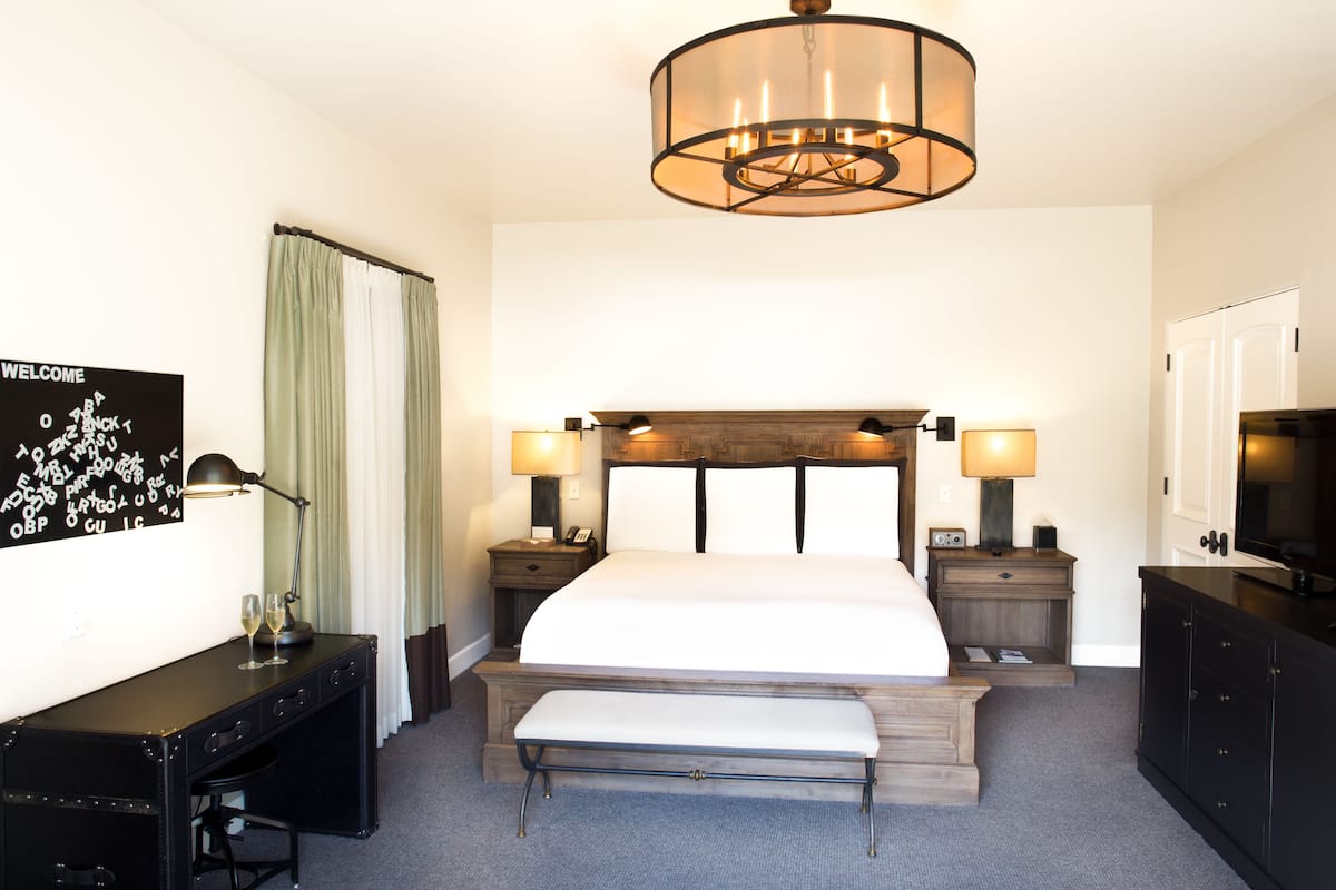 A hotel room with a large bed, bedside lamps, a desk, a bench, a TV, and a 'WELCOME' sign.