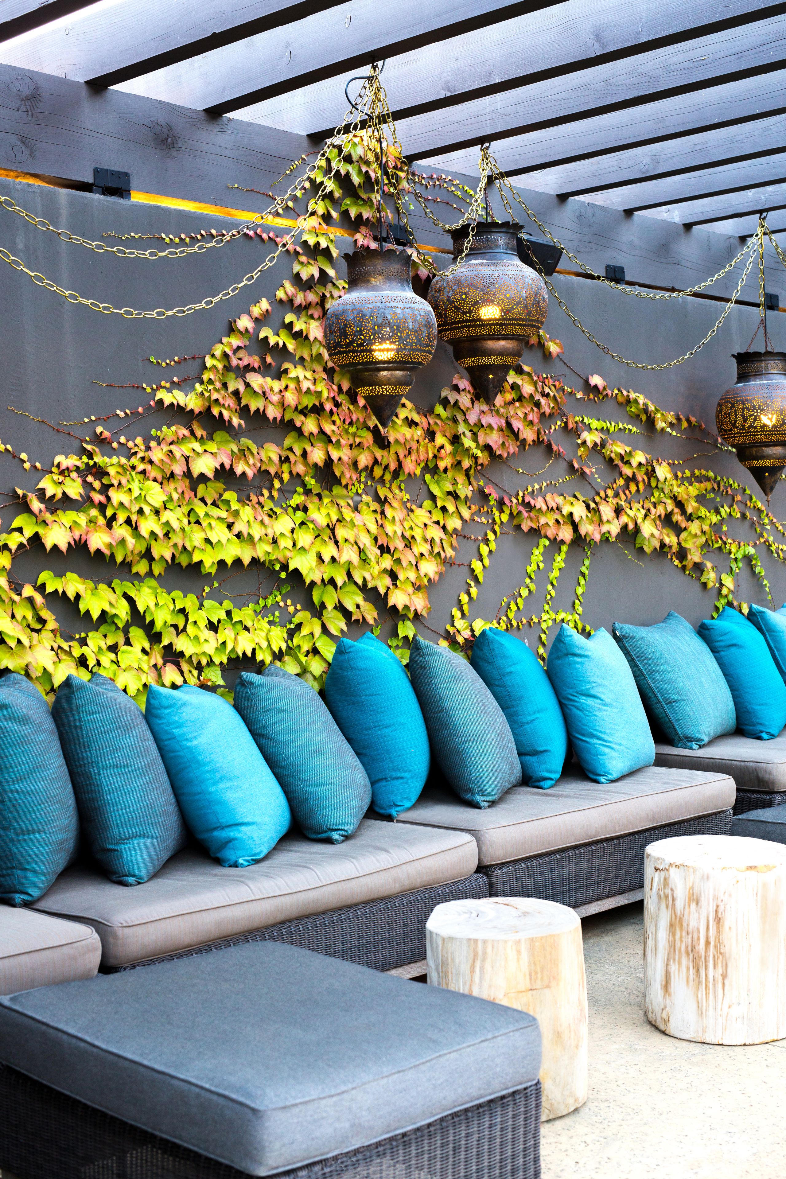 A covered outdoor seating area with a sofa and cushions, a wooden table, and hanging lanterns.