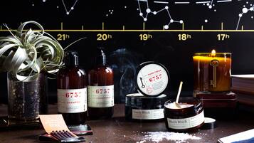 A variety of toiletries on a counter, including shampoo, conditioner, a candle, and a jar of hand cream.