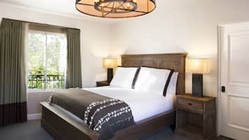 A neatly made bed with a wooden headboard, two bedside tables with lamps, a window with curtains, and a hanging light fixture.