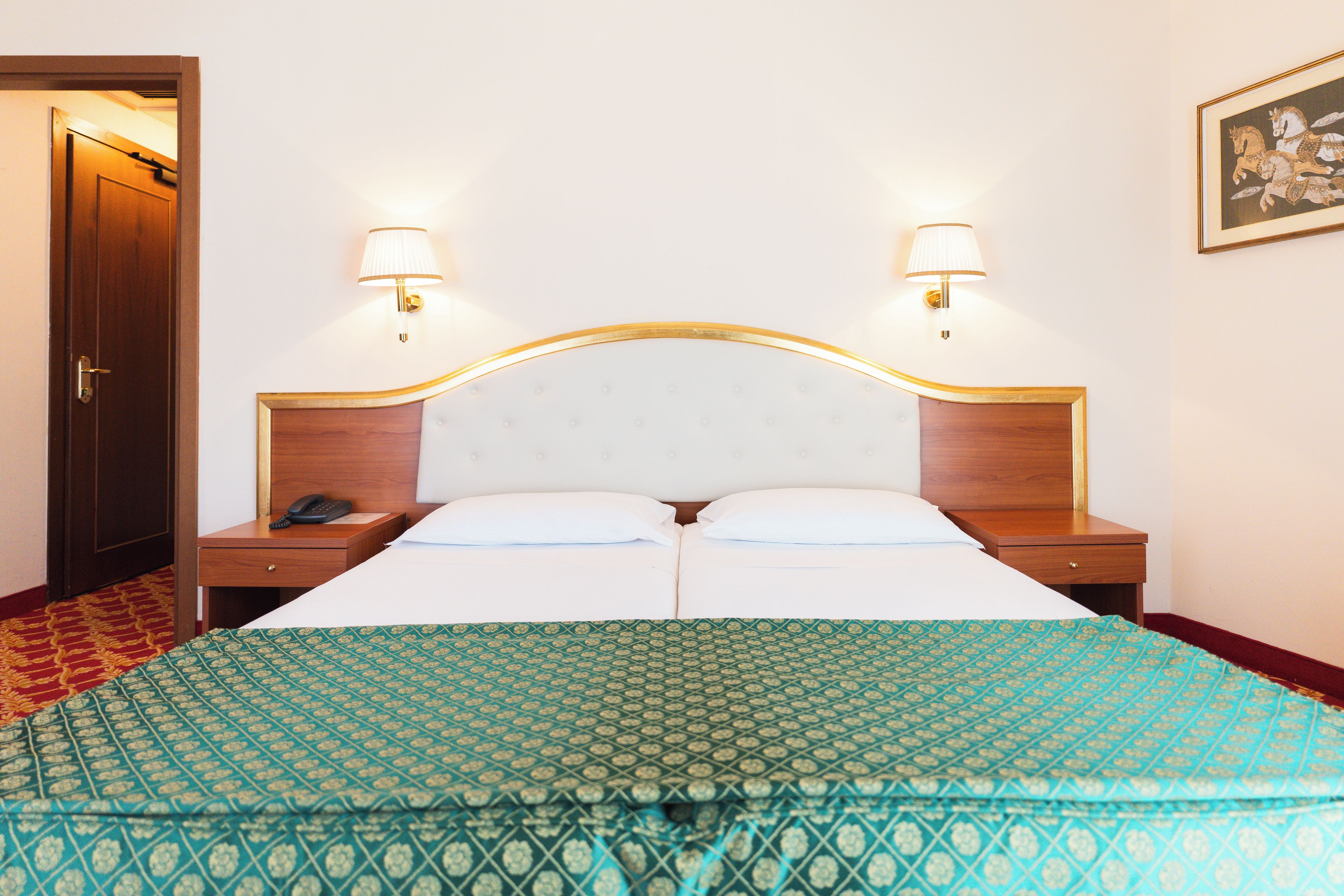 A hotel room with a bed, two bedside tables, a telephone, and two wall-mounted lamps.