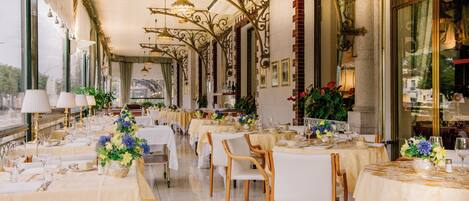 Un restaurant doté de nombreuses tables dressées pour le service, agrémenté d’élégants lustres et de somptueux arrangements floraux.