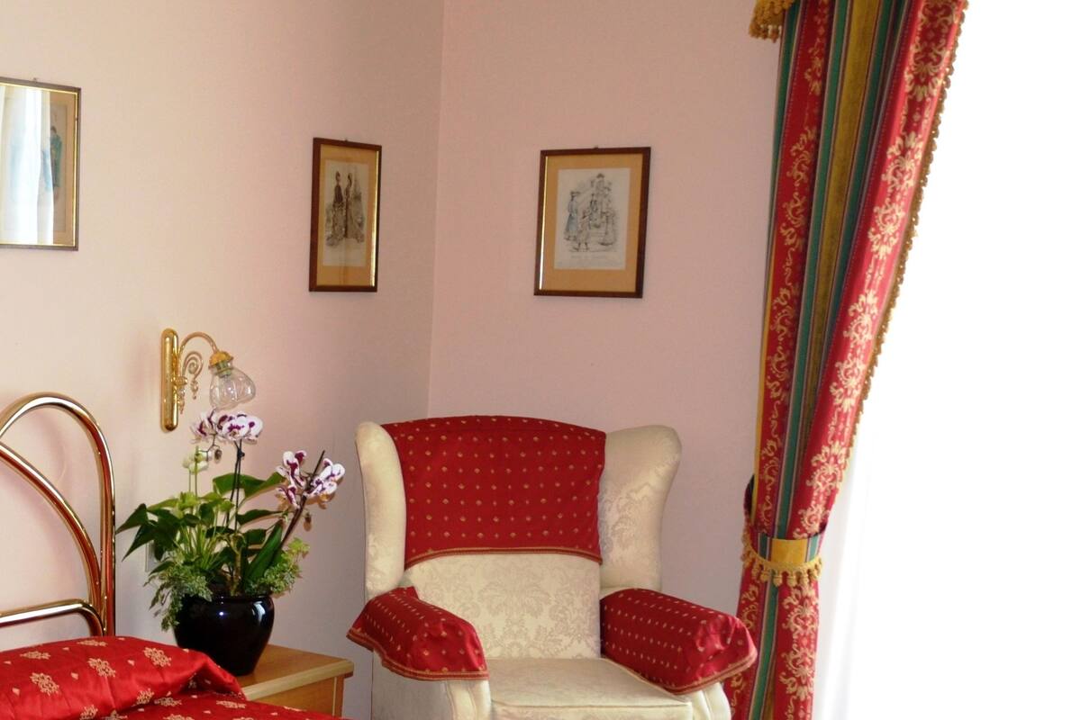Une chambre avec un grand lit, une chaise, une plante en pot et des tableaux encadrés au mur.