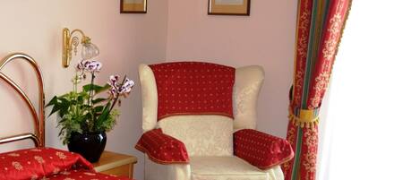 A bedroom with a large bed, a chair, a potted plant, and framed pictures on the wall.