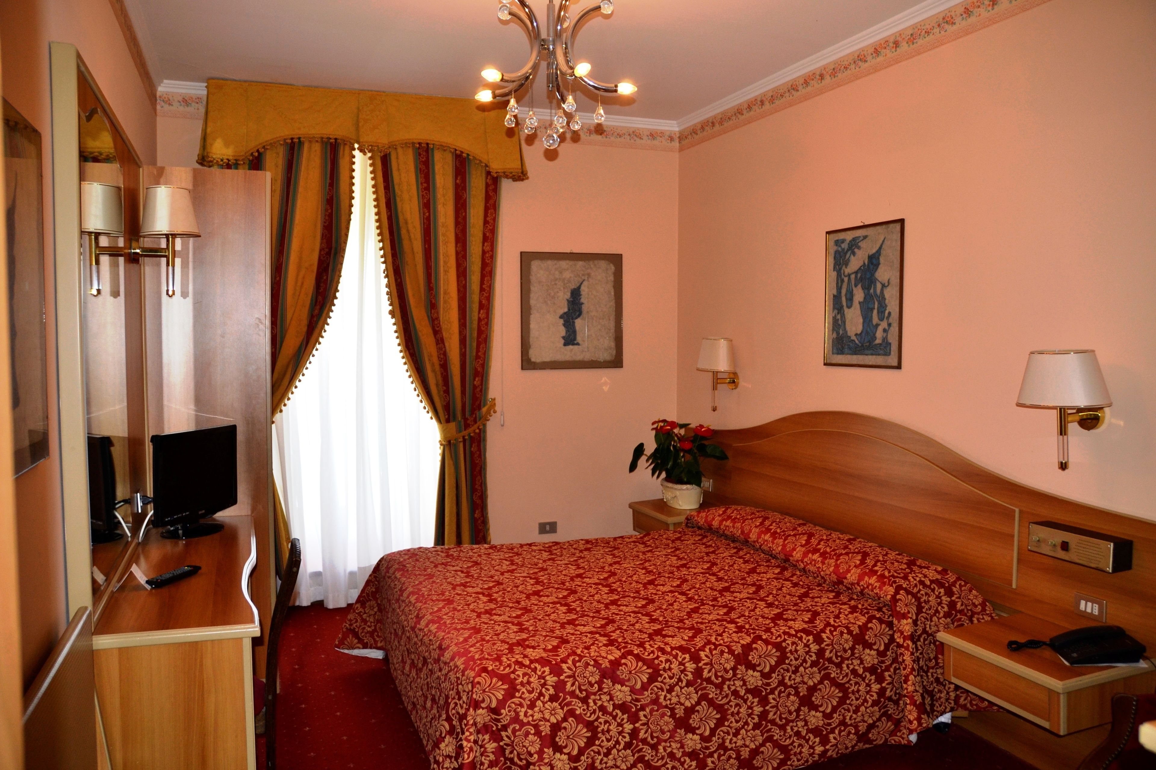 A hotel room with a wooden bed, a desk with a computer, a TV, and a telephone.