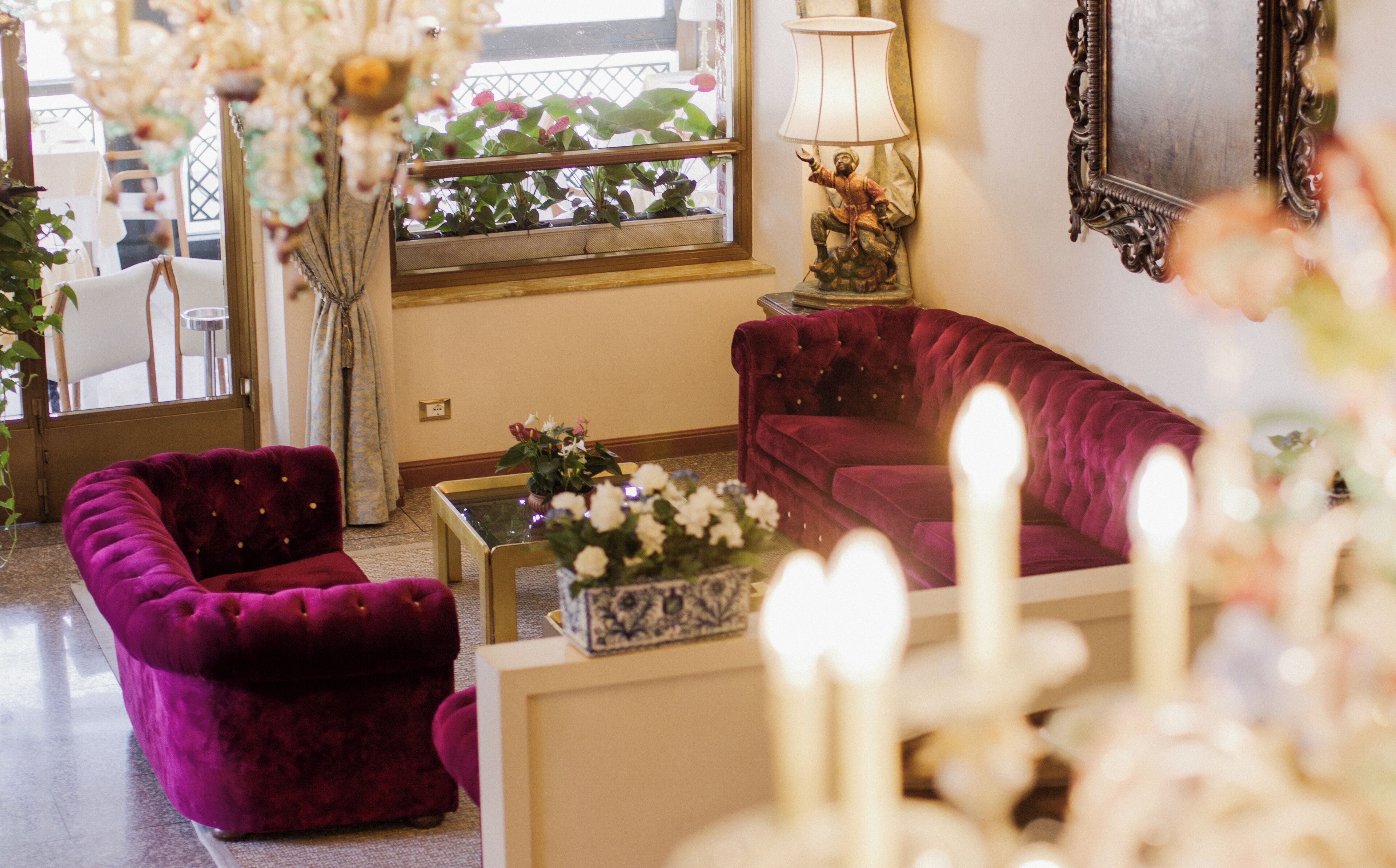 A living room with a purple sofa, a small table with a vase of flowers, and a window with plants.