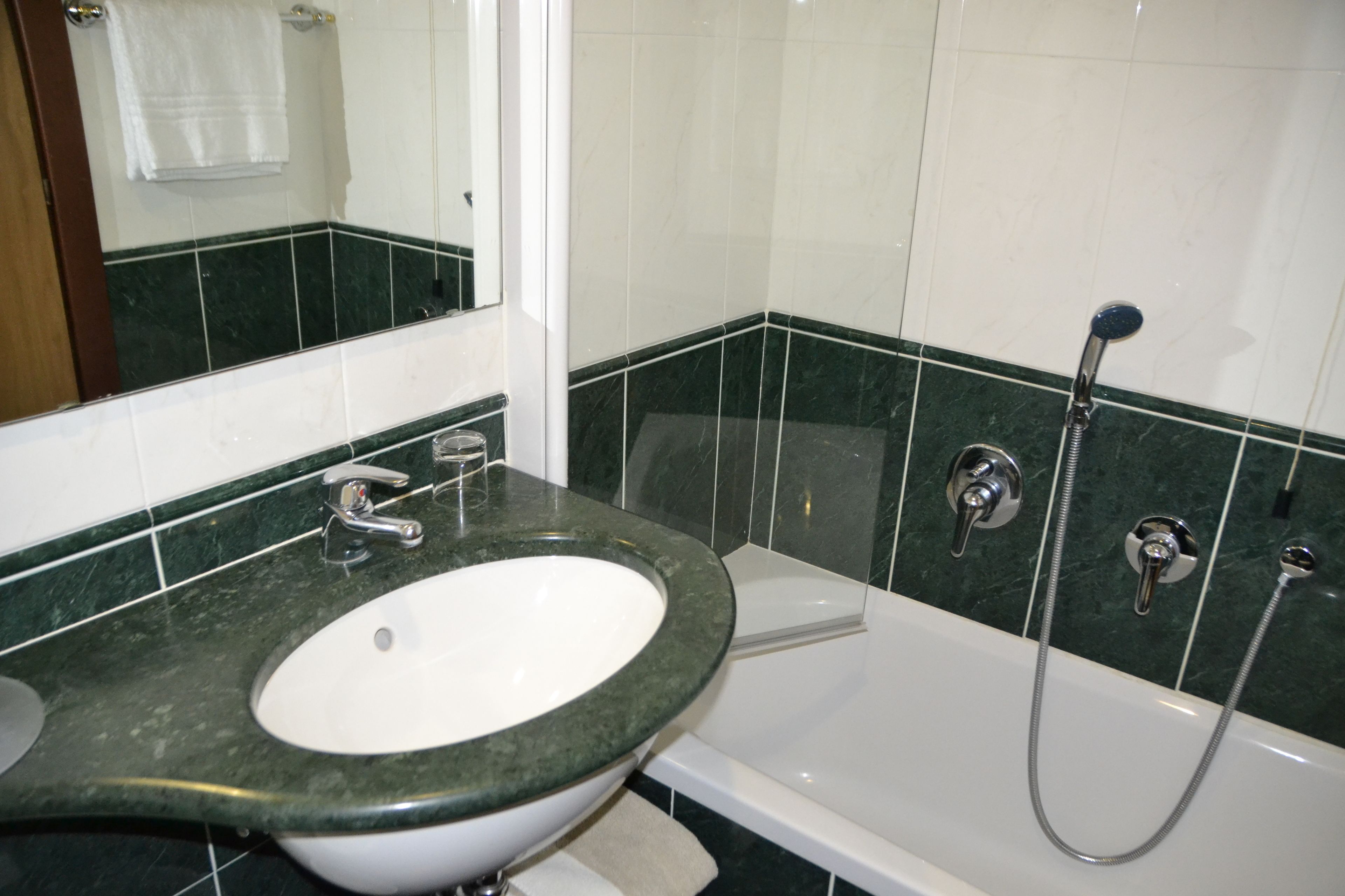 A bathroom with a white sink, a mirror, and a shower with a handheld showerhead.