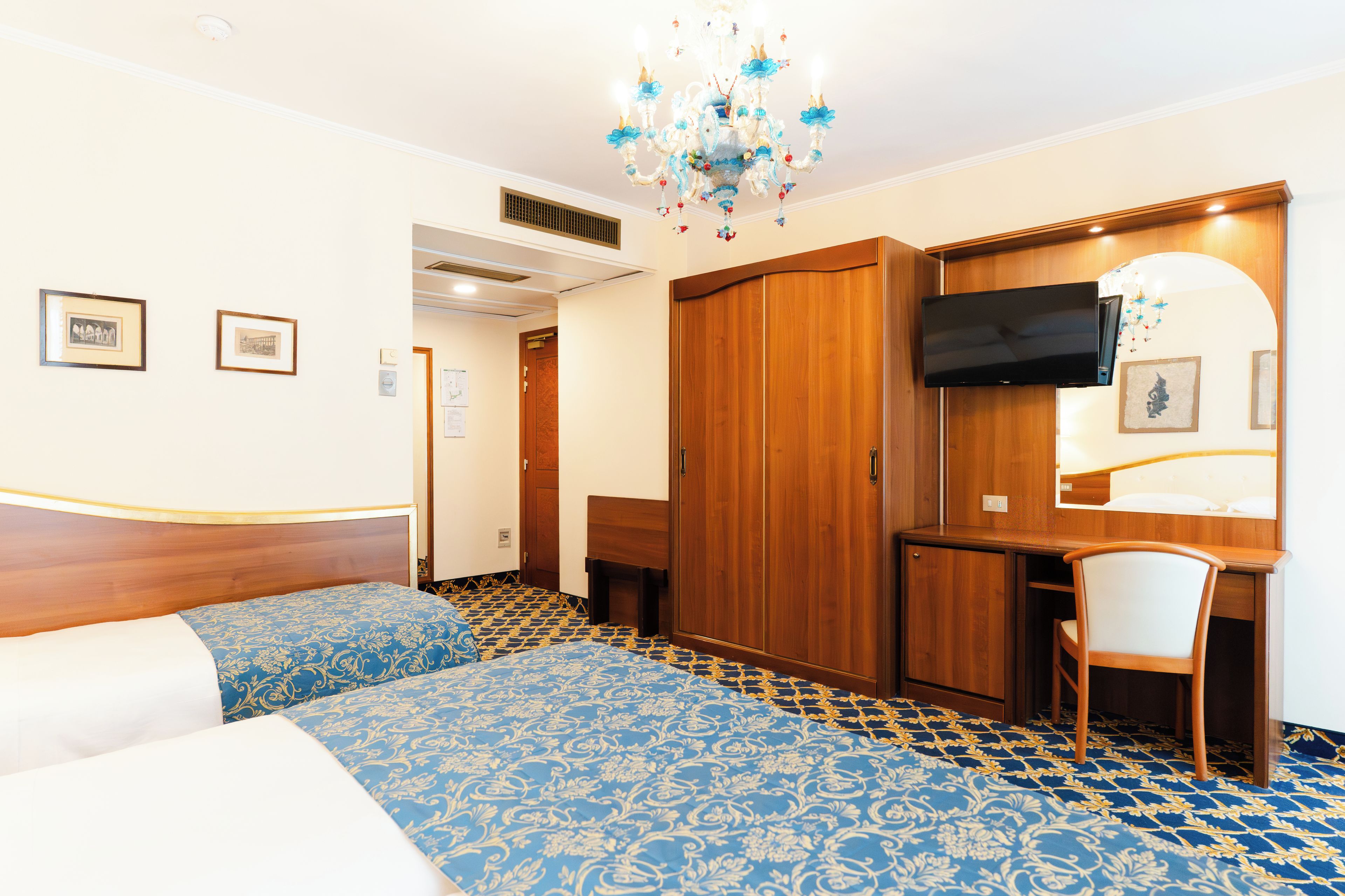 Una habitación de hotel con una cama, un escritorio, una silla, un televisor y una araña.