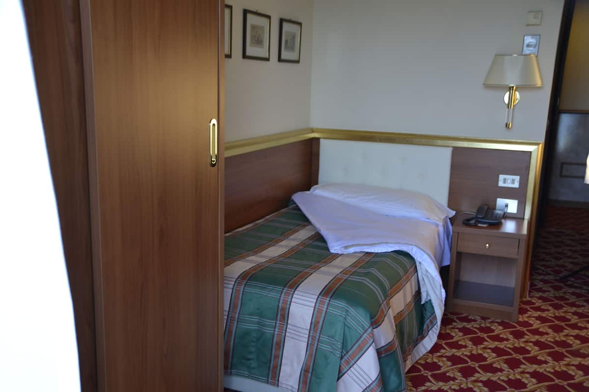 Une chambre d’hôtel avec un lit, une table de chevet avec une lampe et un téléphone fixé au mur.