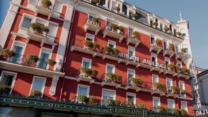 A red and white hotel facade with balconies adorned with flowers, a sign reading "Milan Hotel," and a "Ristorante" sign below. - Hotel Milan Speranza Au Lac (Stresa)