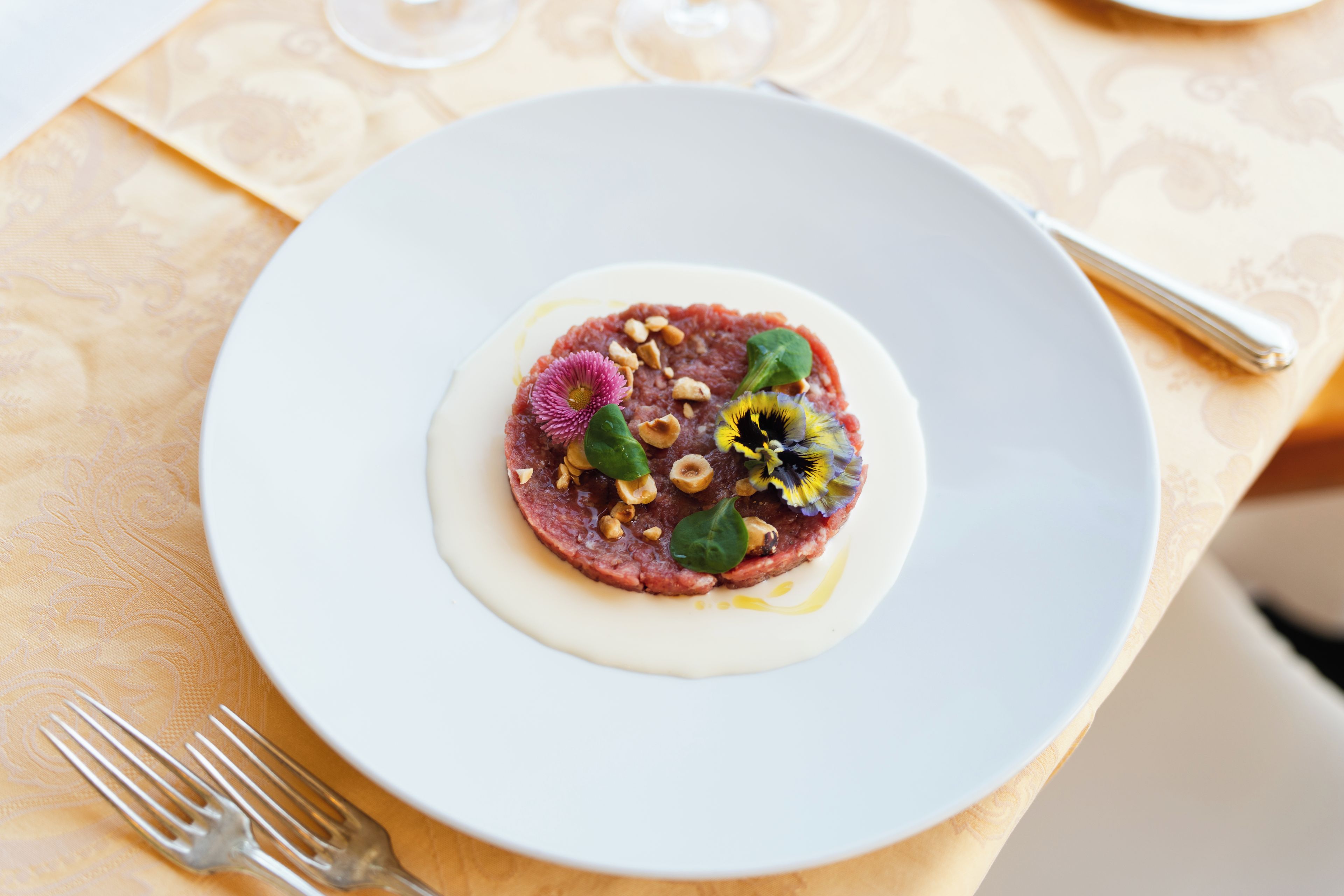 Un plato blanco con un plato de comida, un tenedor y un vaso sobre una mesa con mantel estampado.