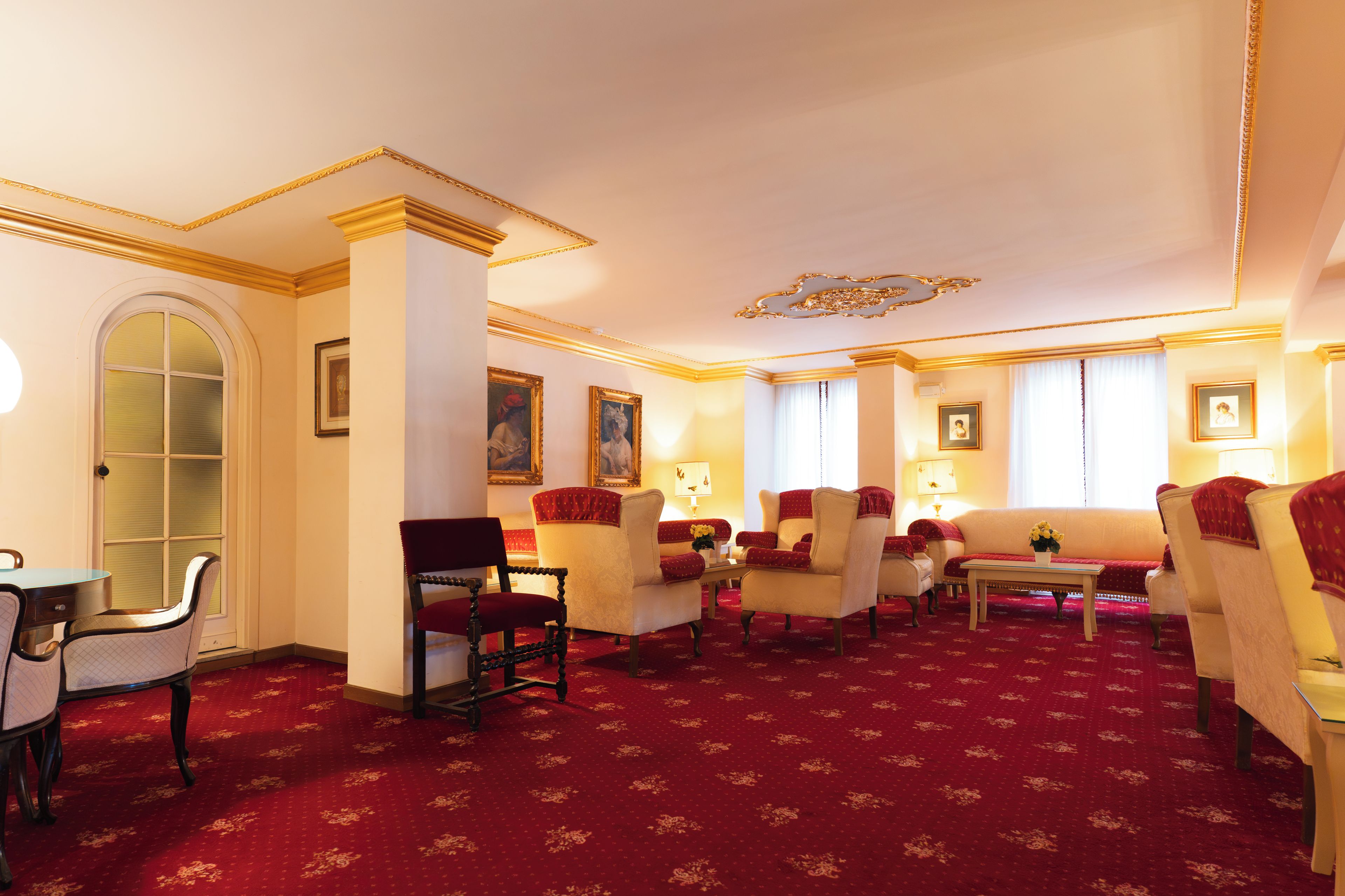 Un hall d’hôtel avec un tapis rouge, plusieurs espaces aménagés pour s’asseoir et des œuvres d’art encadrées qui ornent les murs.