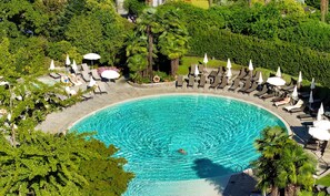Une grande piscine circulaire, entourée de chaises longues et de parasols, avec une végétation luxuriante en arrière-plan.