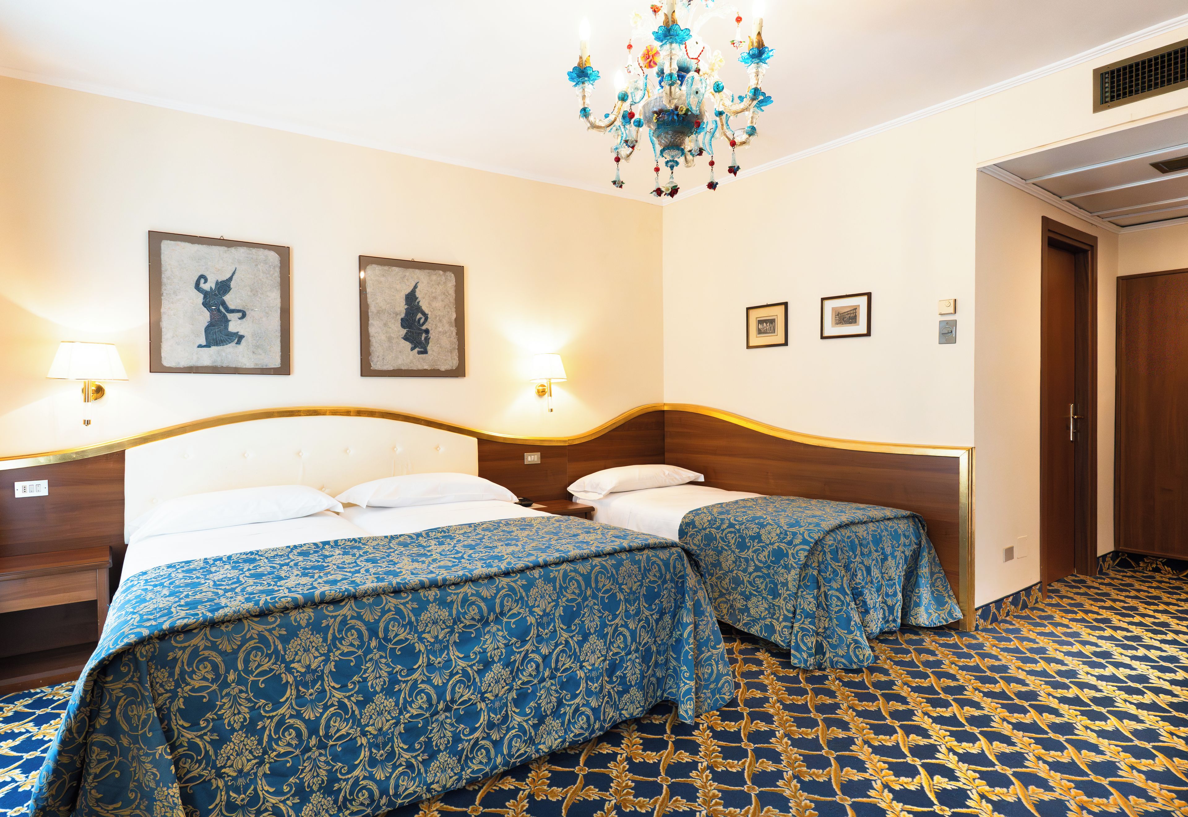 A hotel room with two beds, a chandelier, and artwork on the walls.