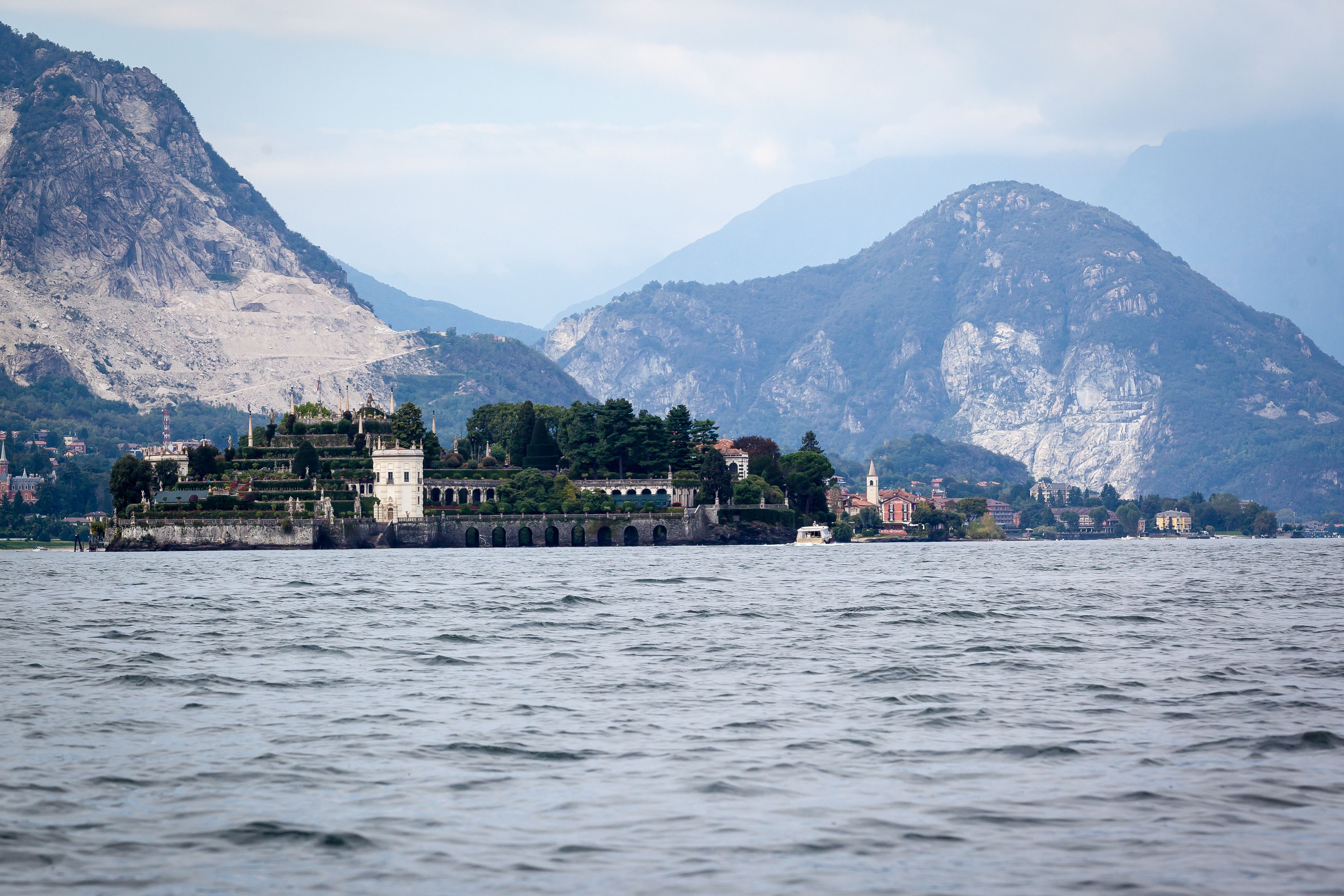 A historic building with a fortified structure and a tower, located by a body of water with mountains in the background.