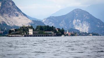 A historic building with a fortified structure and a tower, located by a body of water with mountains in the background.