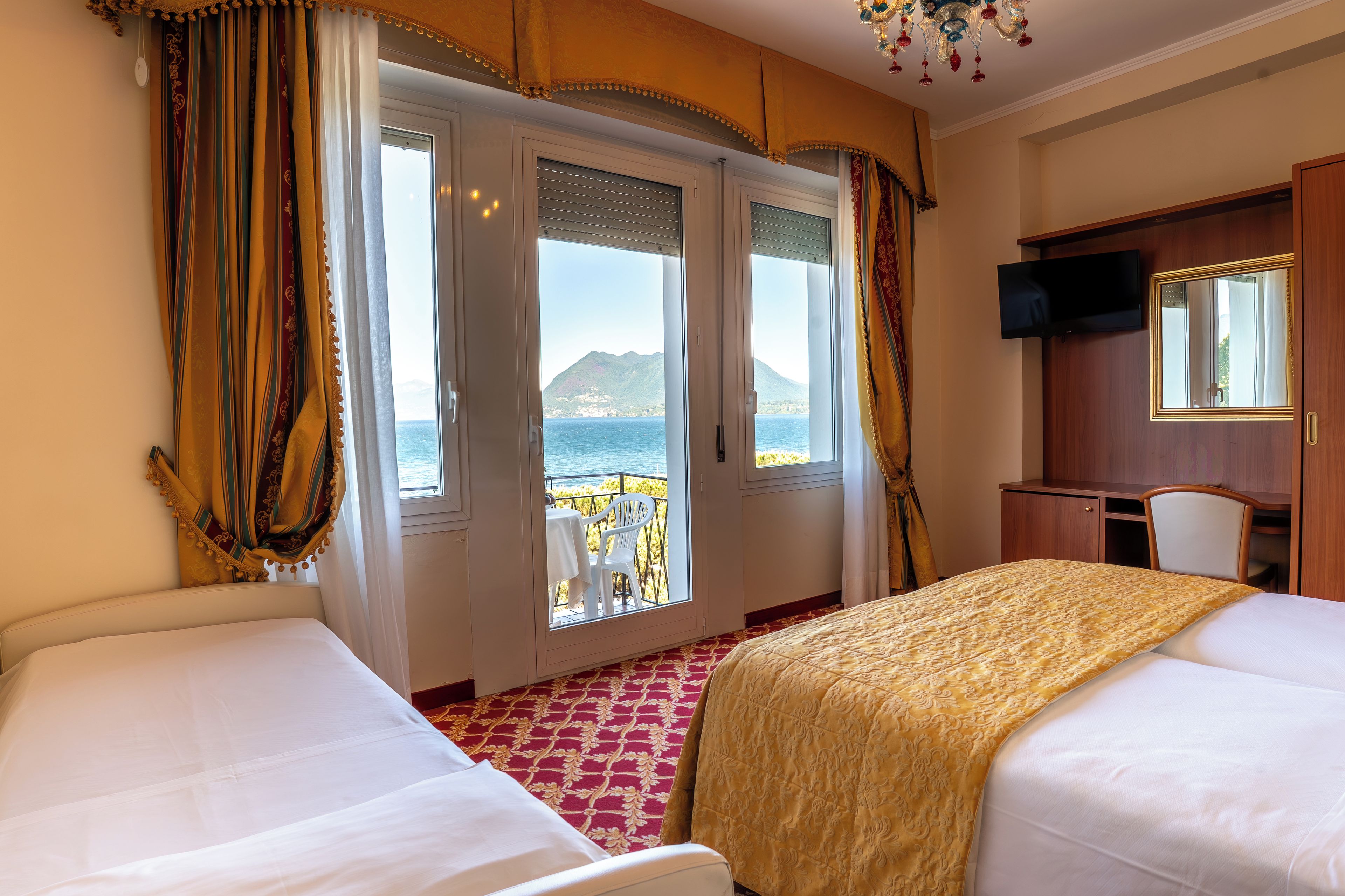 A hotel room with two beds, a TV, and a balcony with a view of the sea.