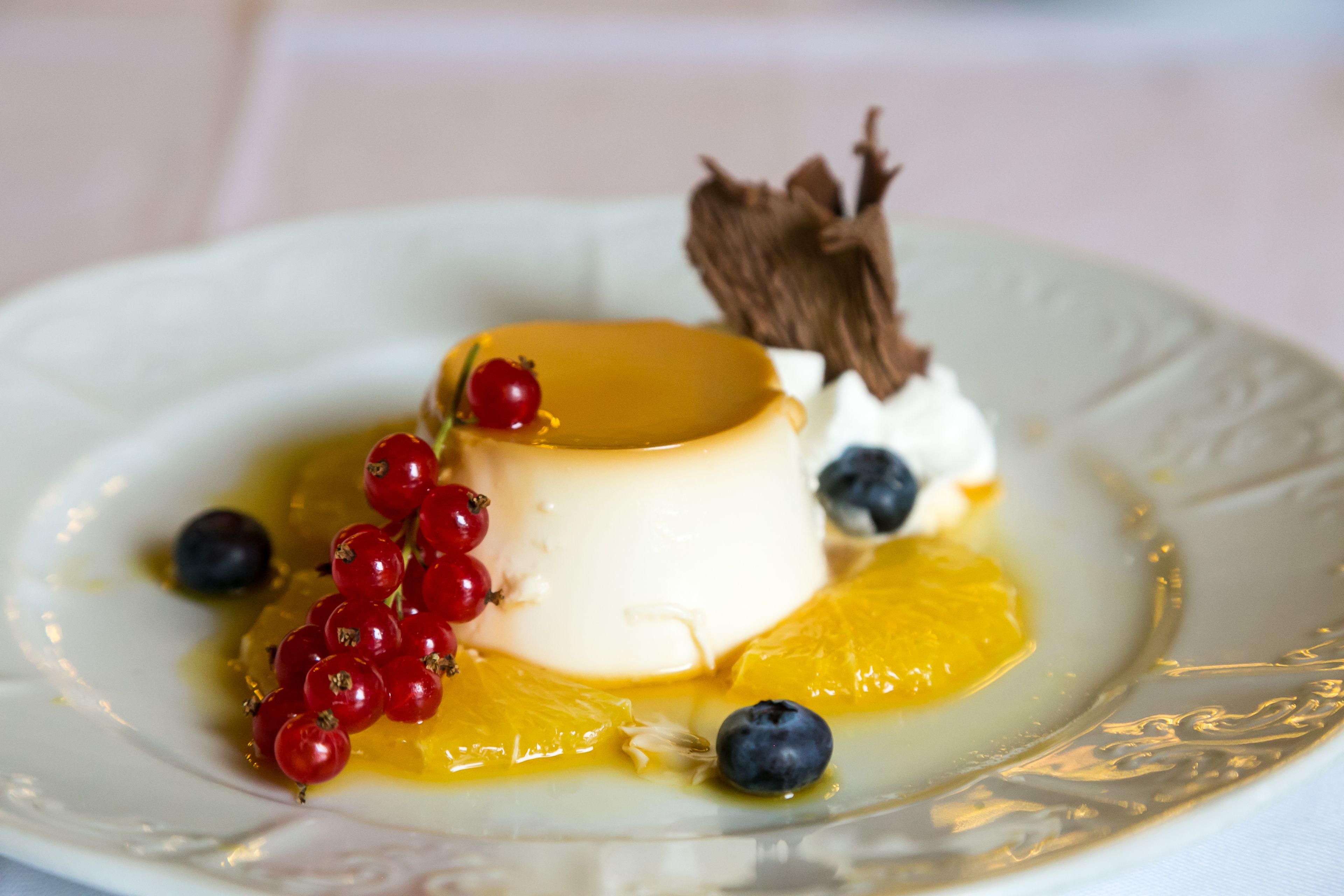 A dessert with a caramelized top, surrounded by red currants and blueberries, on a white plate.