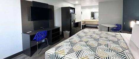 A modern hotel room with a bed, a desk with a chair, a TV, a wardrobe, and a small table with a chair.