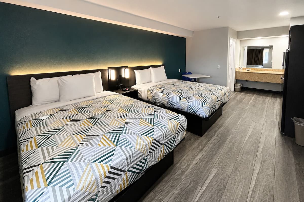 Une chambre d’hôtel avec deux lits, une petite table, un miroir et une salle de bain visible à travers une porte ouverte.