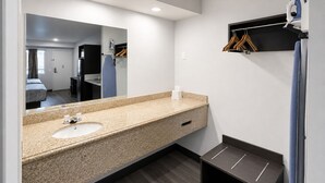 A modern bathroom with a granite countertop sink, a mirror, a towel rack, and a small shelf. - Value Stay Inn Extended Stay Bakersfield (Bakersfield)