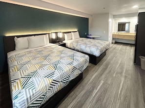 Ein Hotelzimmer mit zwei Betten, einem kleinen Tisch, einem Spiegel und einem durch eine geöffnete Tür einsehbaren Badezimmer.