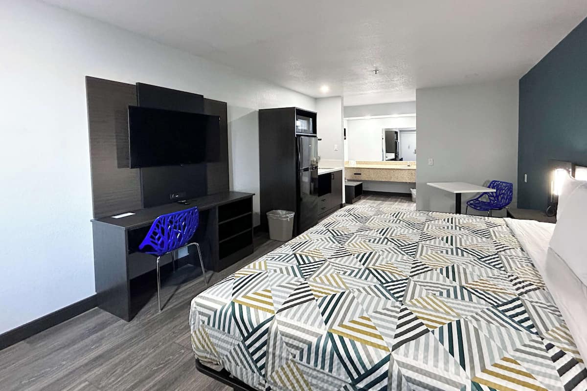 Une chambre d’hôtel moderne dotée d’un grand lit, d’un bureau avec une chaise, d’un téléviseur fixé au mur et d’un petit coin cuisine.